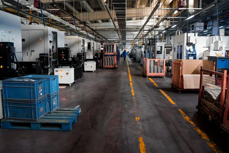 A long factory aisle lined with machines, blue crates and parts trolleys under strip lights.